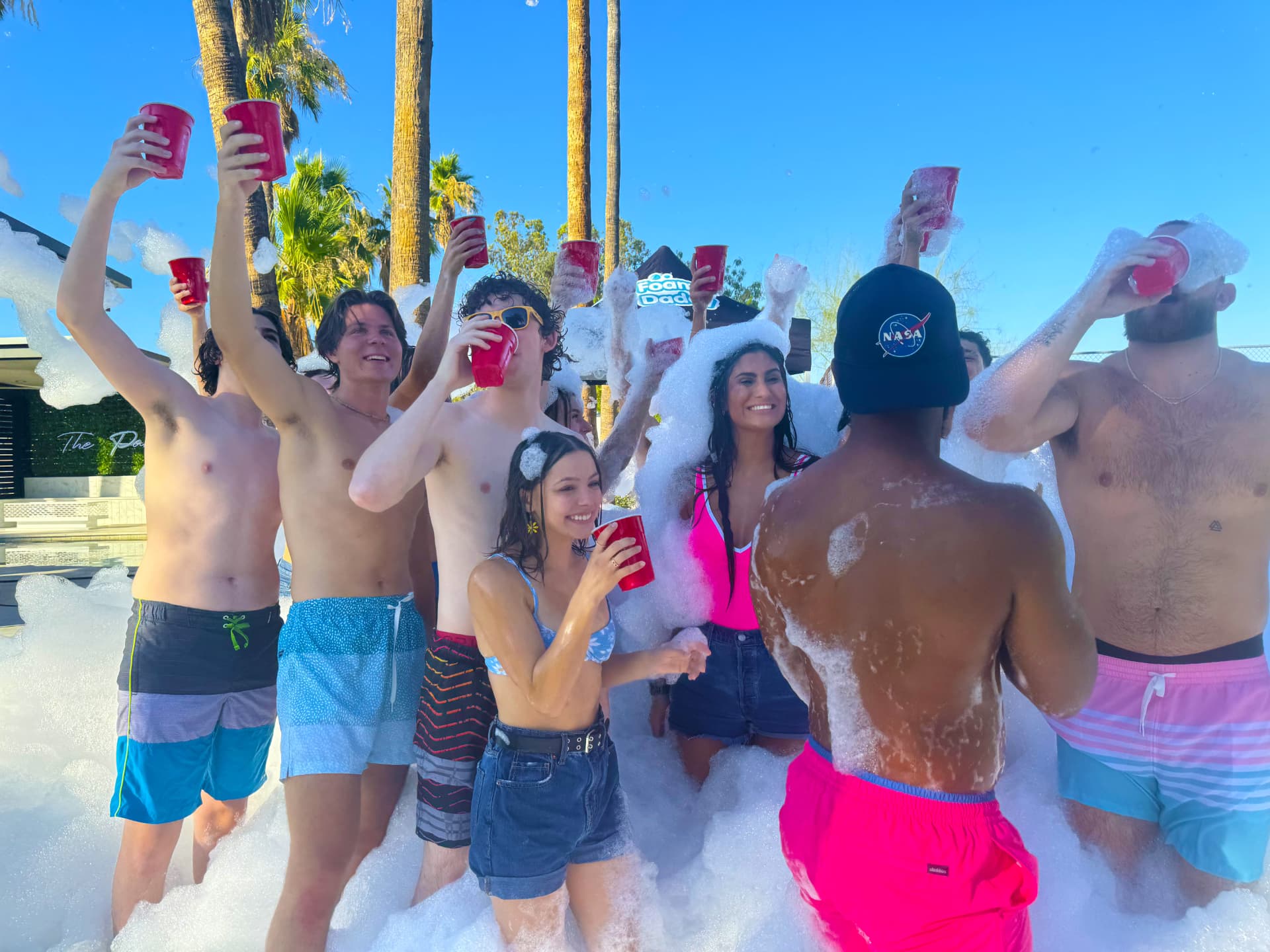College students raising cups and celebrating in foam at an outdoor foam party