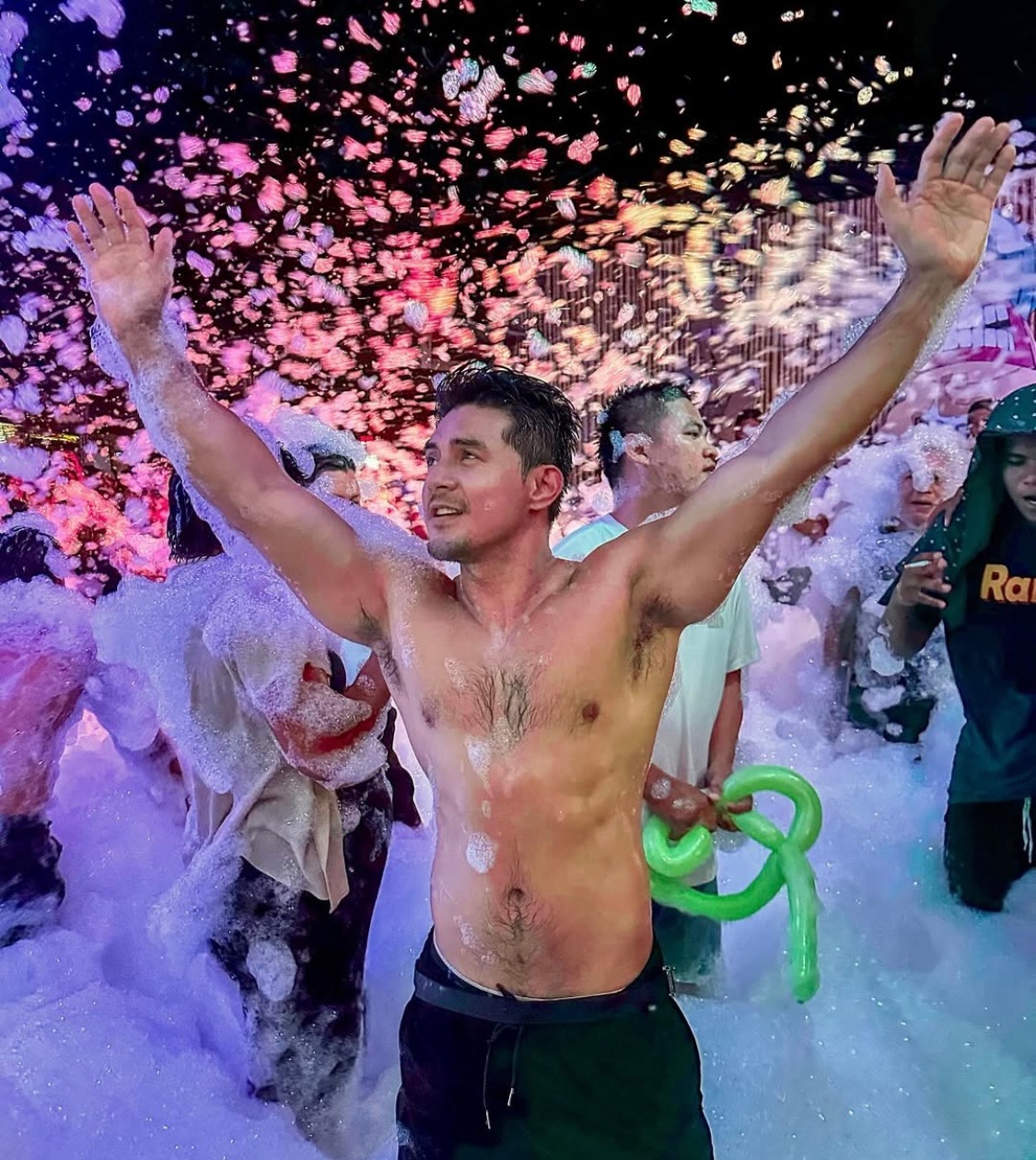 Crowd with hands in the air under pink and purple glow foam at a late-night event