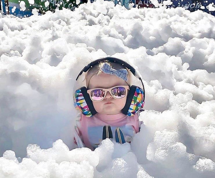 Baby in sunglasses and ear protection surrounded by foam at a family event