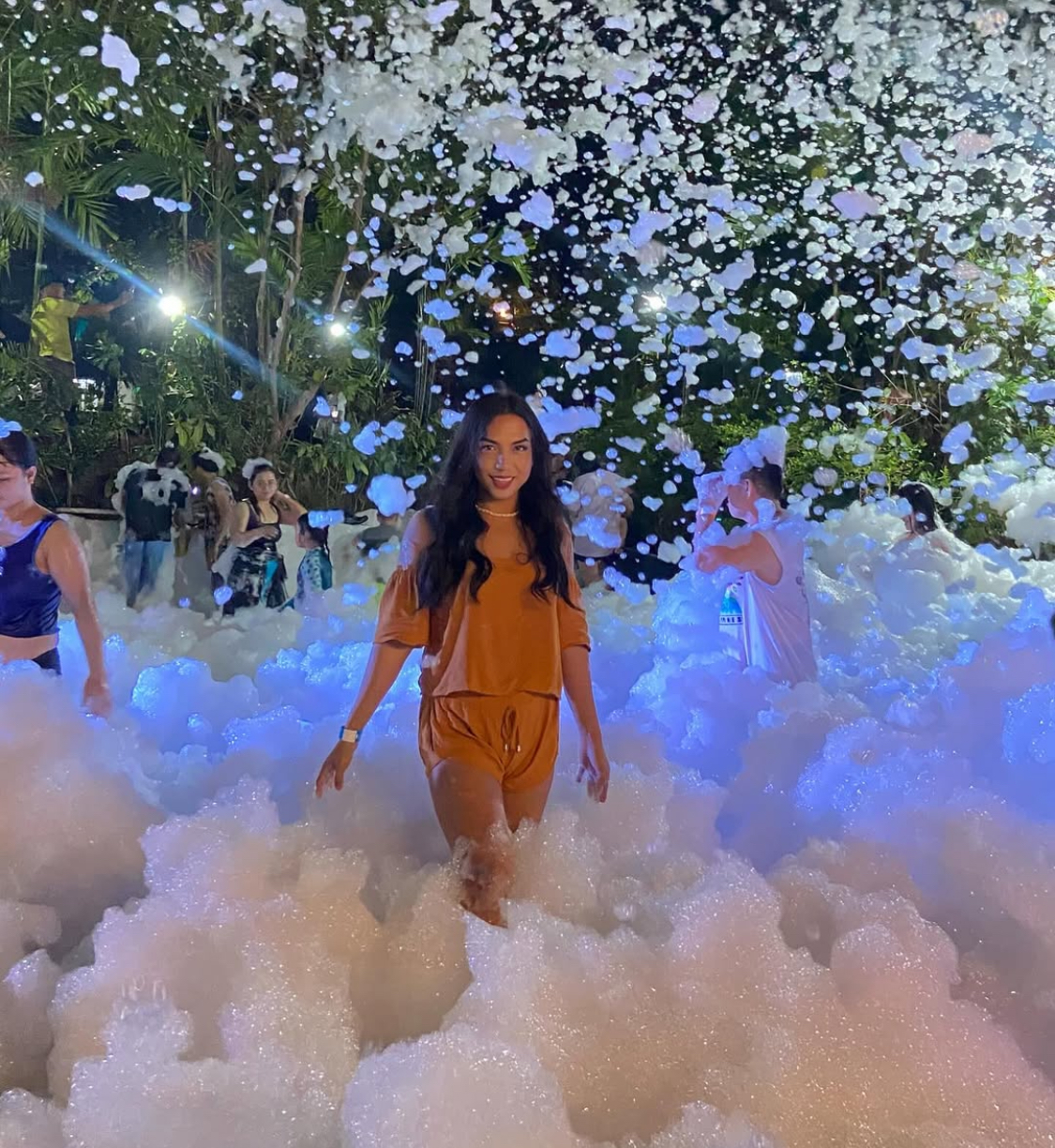 Guest walking through waist-deep glowing foam at an outdoor nighttime foam party