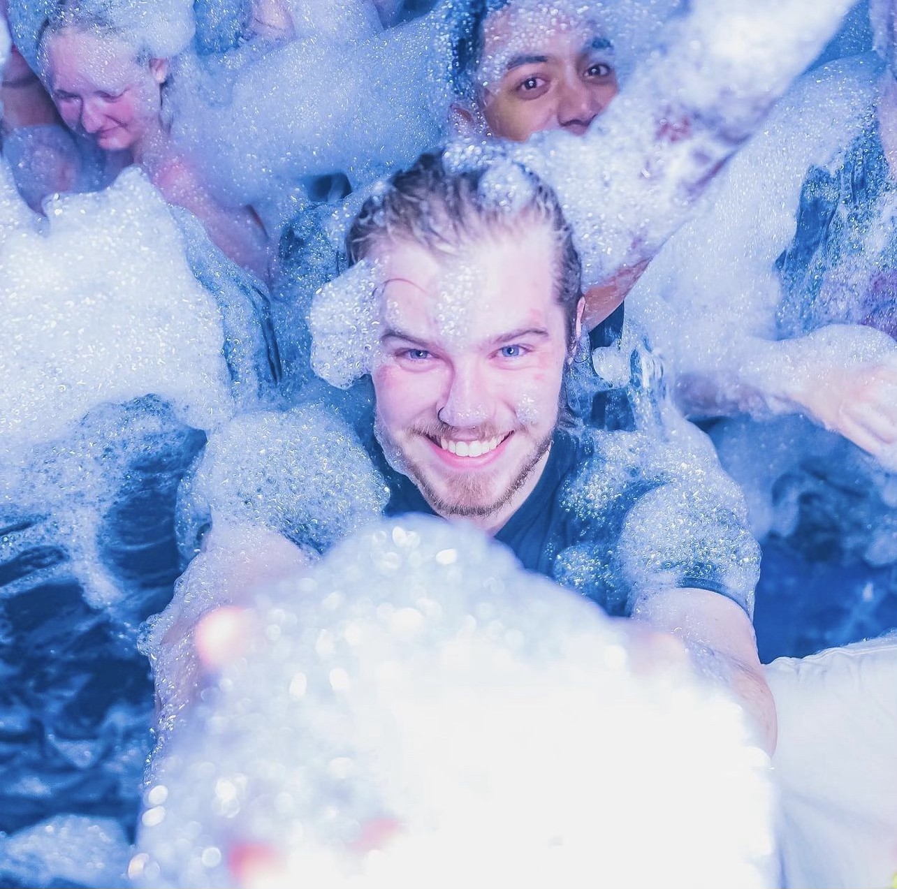 Guest laughing while buried in blue-lit foam at a special event