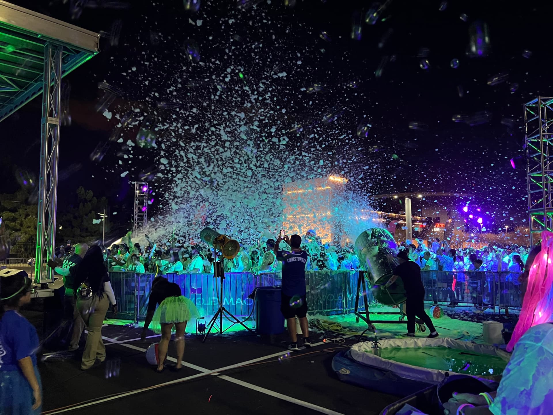 Foam cannons blasting glowing foam over a barricaded community event crowd at night